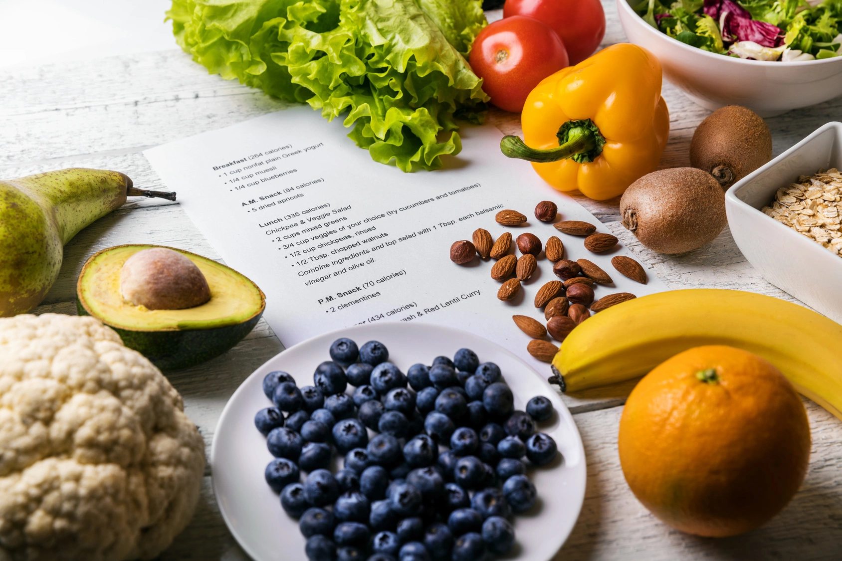 Dieta OXY - na czym polega i jak ją stosować? Owoce, warzywa i orzechy leżą na stole obok jadłospisu.