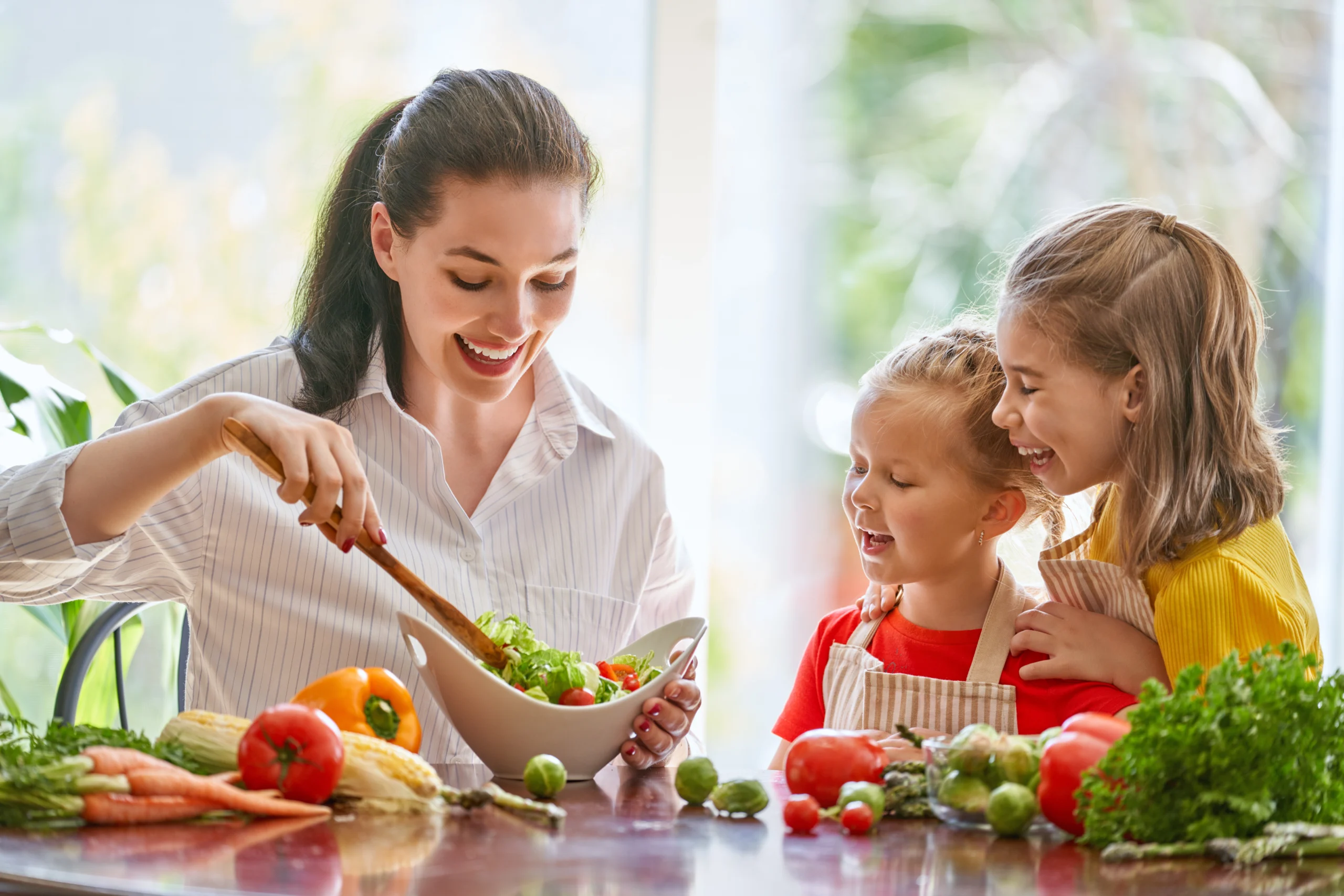 Dobre nawyki żywieniowe u dzieci - mama gotuje w kuchni z dwiema córeczkami.