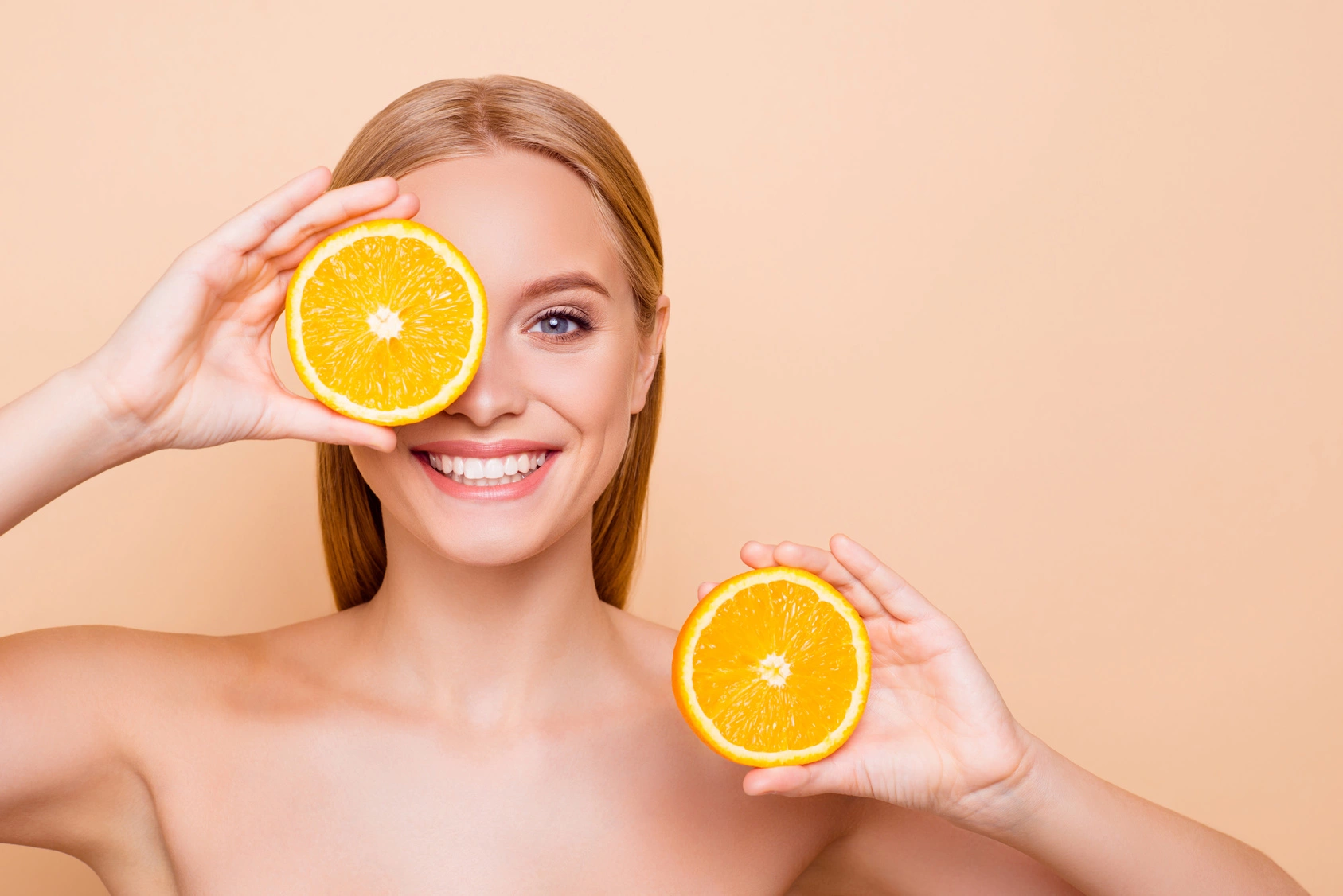 Dieta na cerę - jaka najlepsza? Kobieta trzyma w rękach dwie połówki pomarańczy, przykłada jedną z nich do oka.