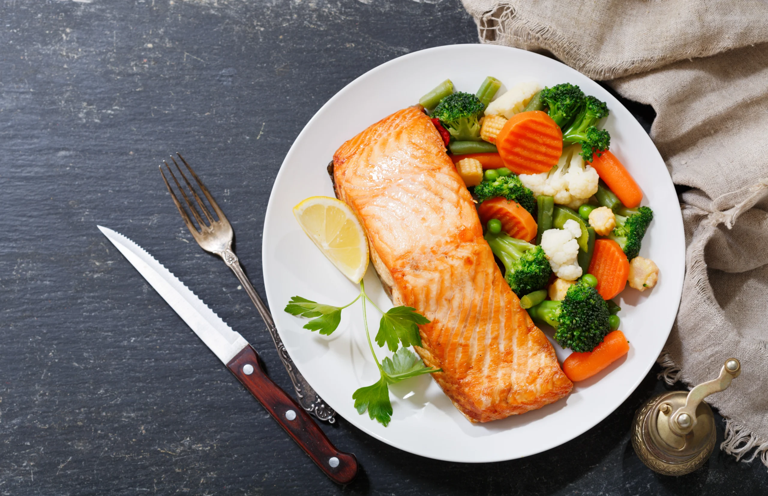 Najzdrowsze ryby - jakie warto jeść? Pieczony łosoś z warzywami na białym talerzu na betonowej powierzchni.