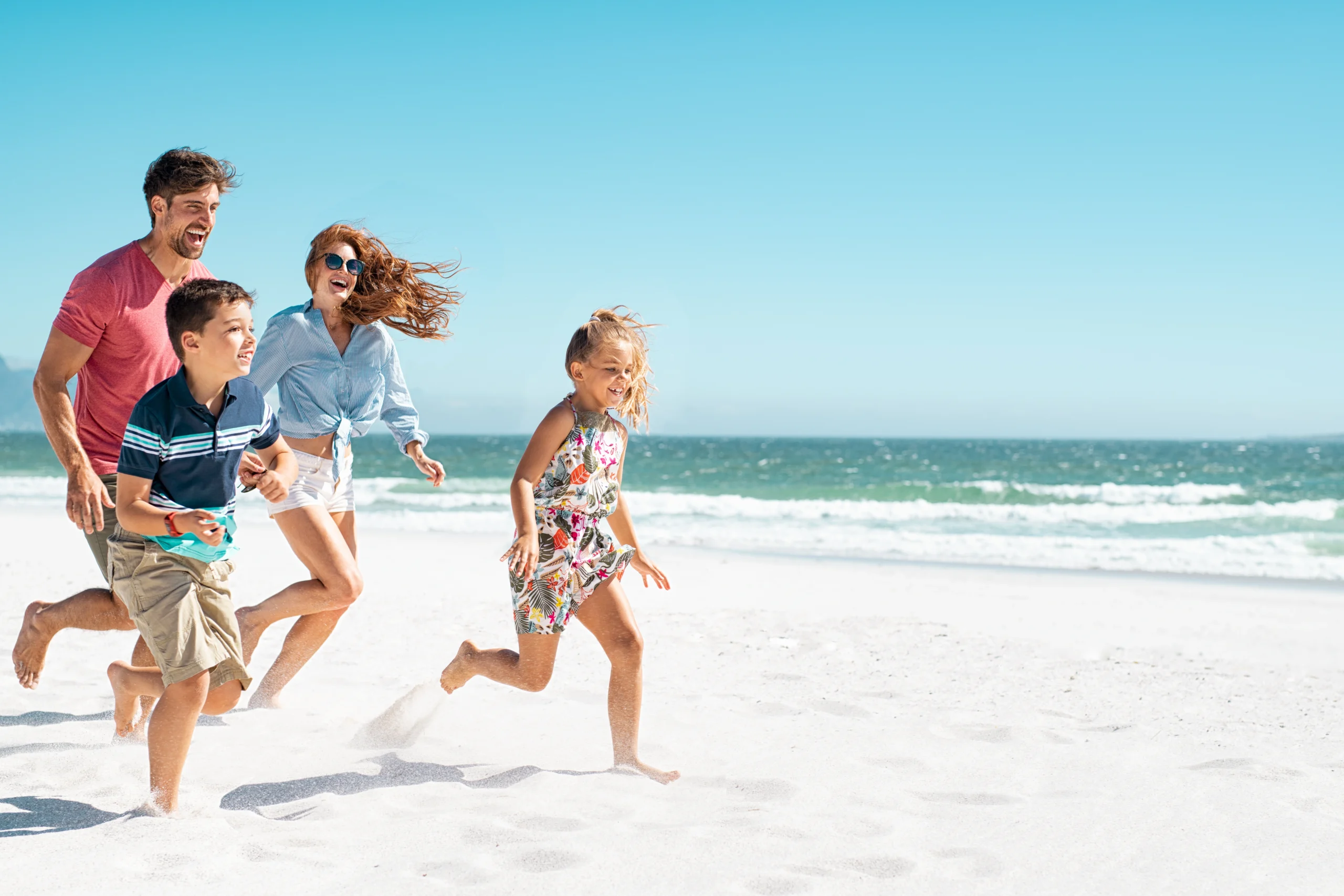 Jakie witaminy brać latem? Czy warto suplementować wit D, C i A latem? Rodzina biega po plaży w letni dzień.