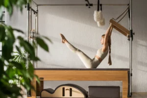 Młoda kobieta w beżowym stroju sportowym trenuje pilates na reformerach w studiu treningowym.